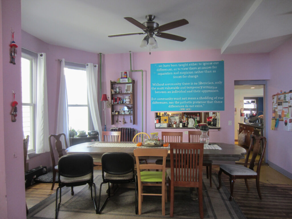 Table surrounded by chairs sits in the middle of a pink dining room in front of a mural.