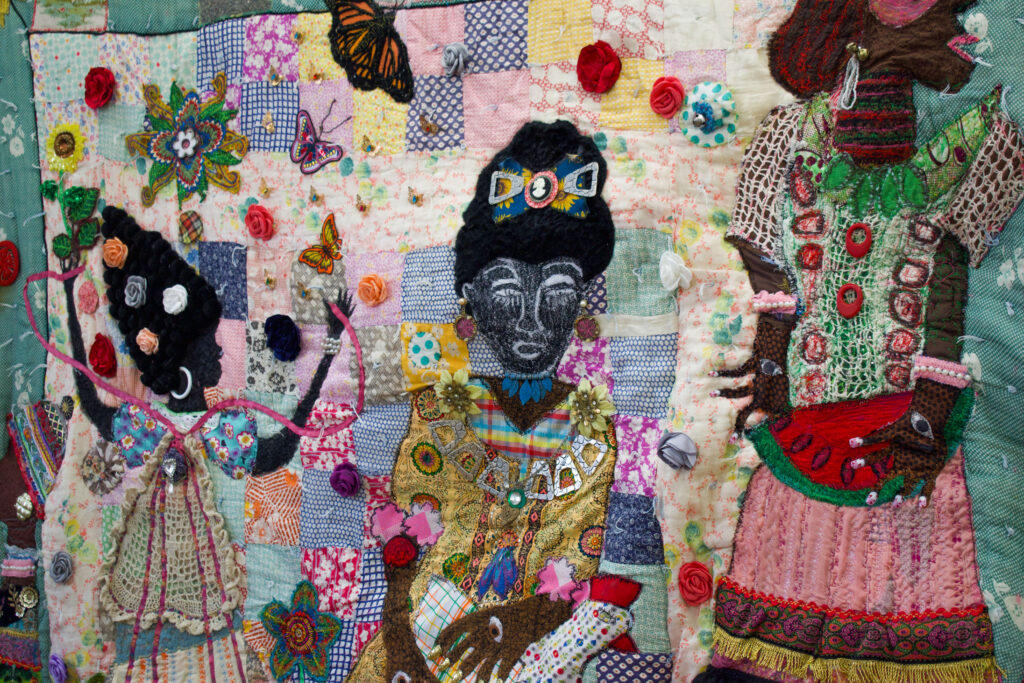 Colorful quilt decorated with three women wearing ornate jewelry and dresses.